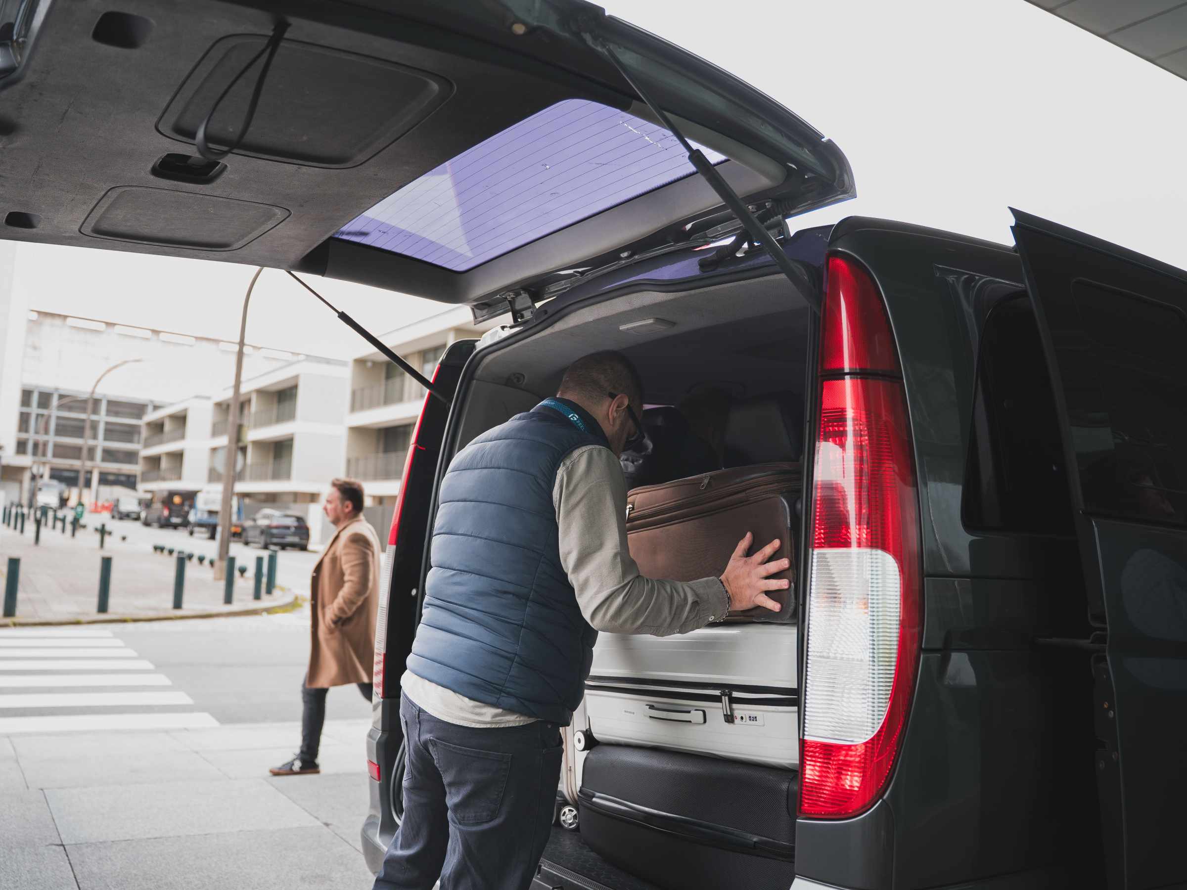 Man loading luggage into the back of a van on a city street.