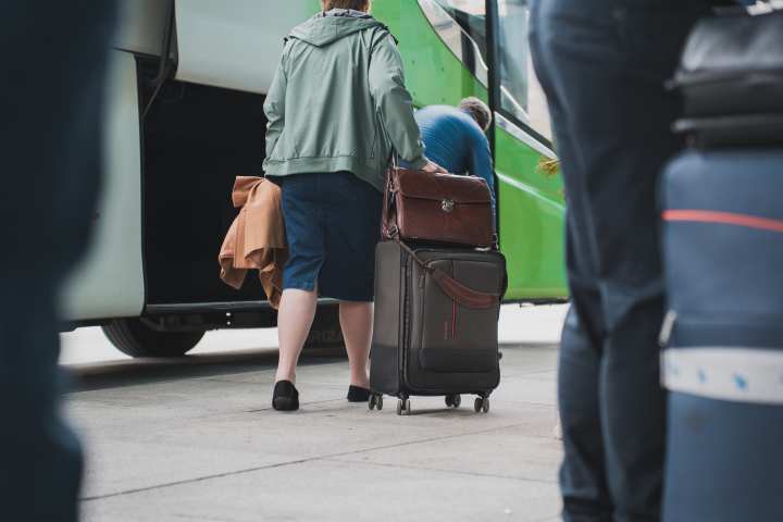 Person in green jacket boarding a bus with a suitcase.