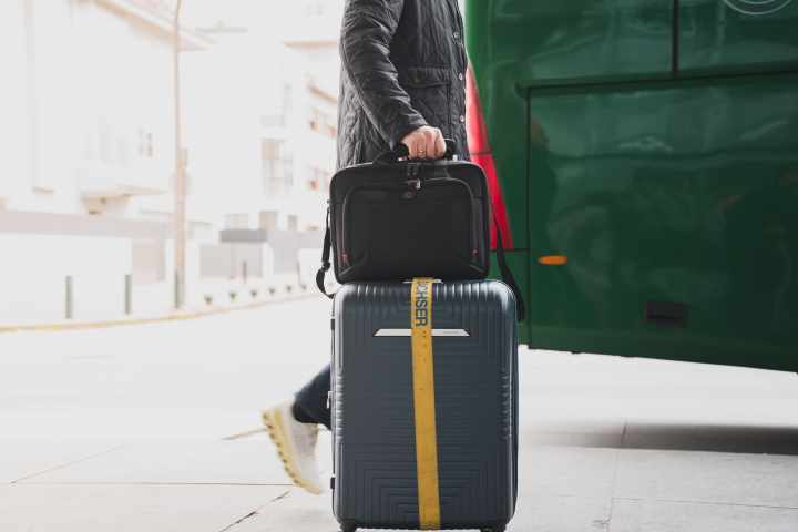 Person with suitcase and briefcase near a green bus.