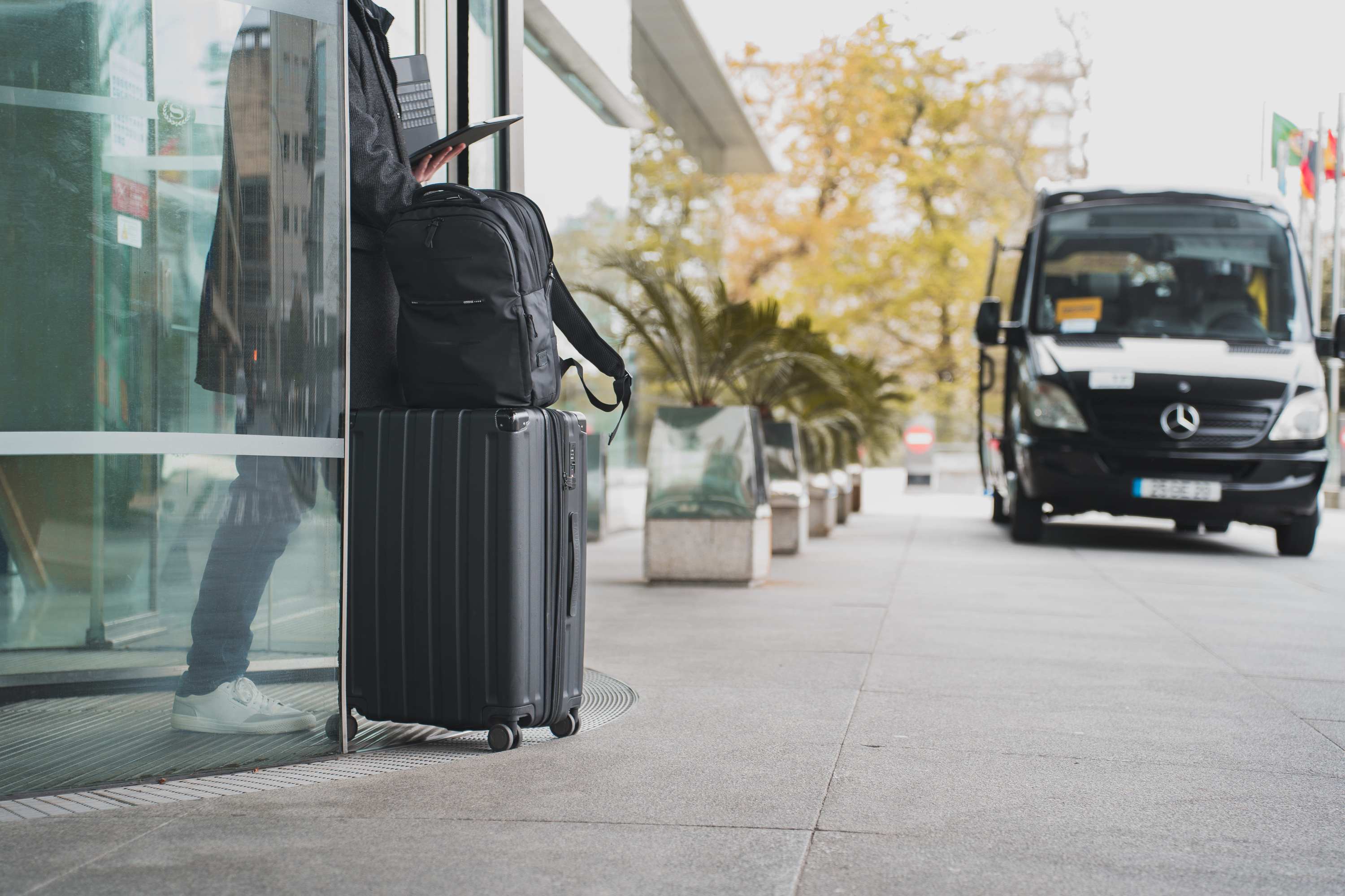 Person with luggage waits by glass door near parked van.