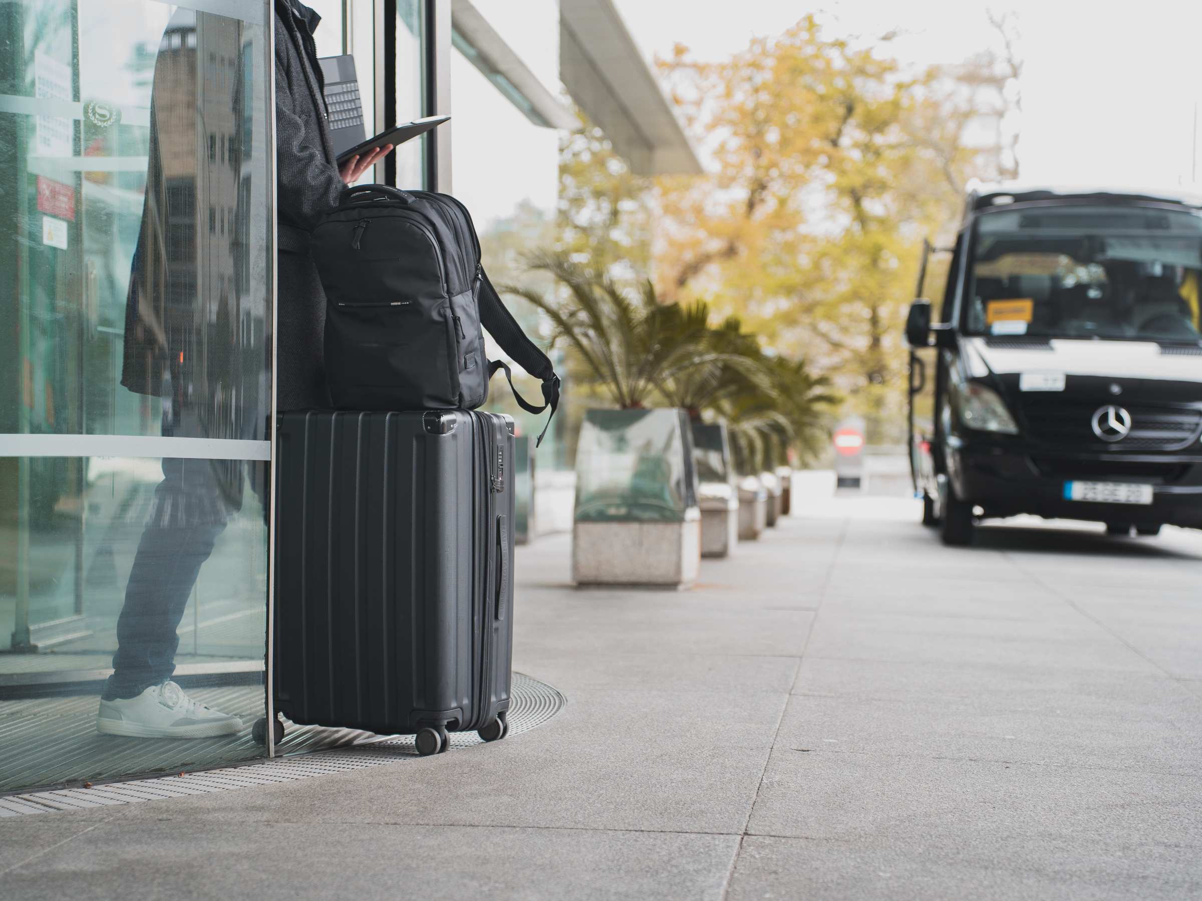 Person with luggage waits by glass door near parked van.