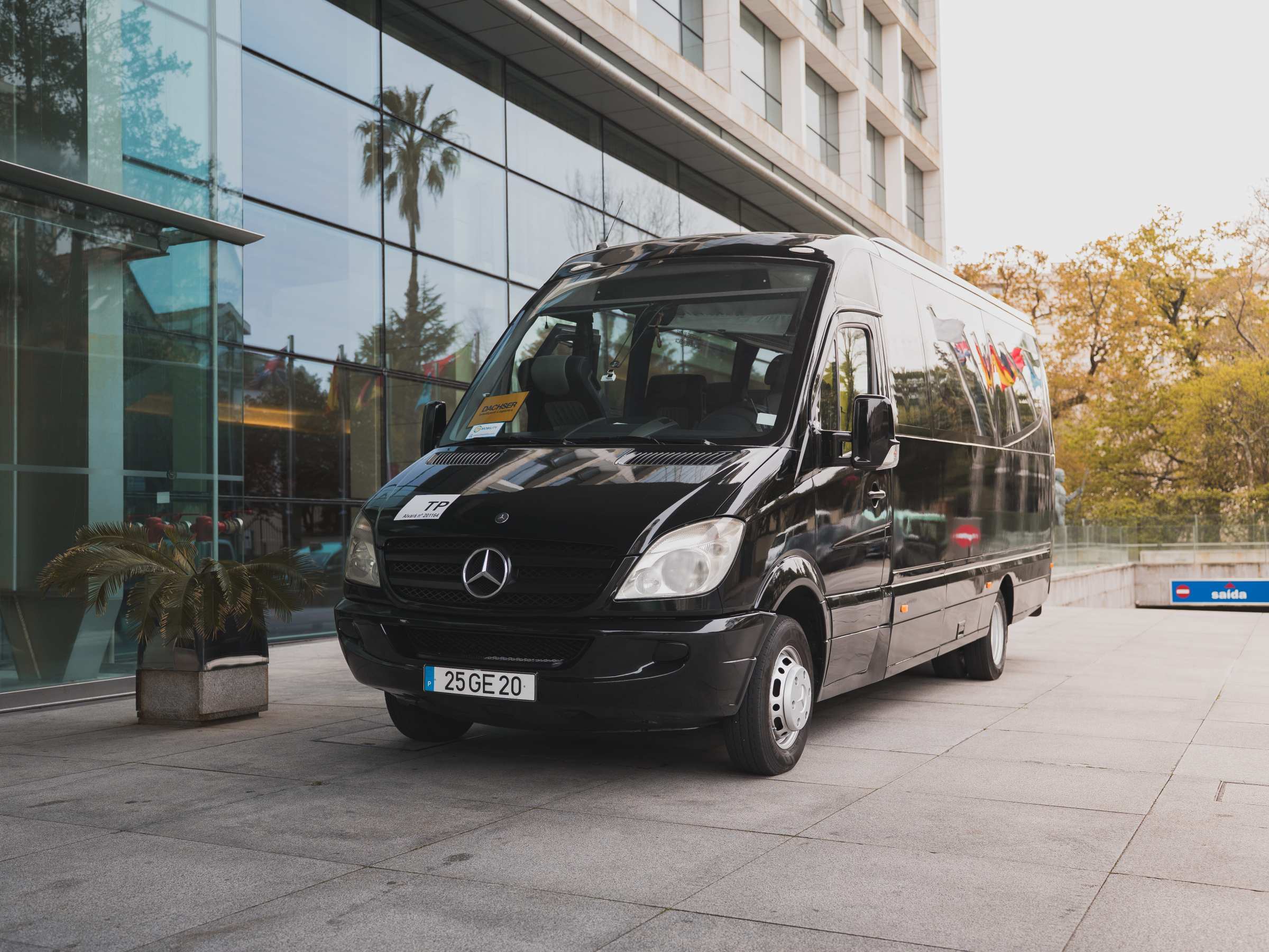 Black van parked outside a modern glass building with trees in the background.