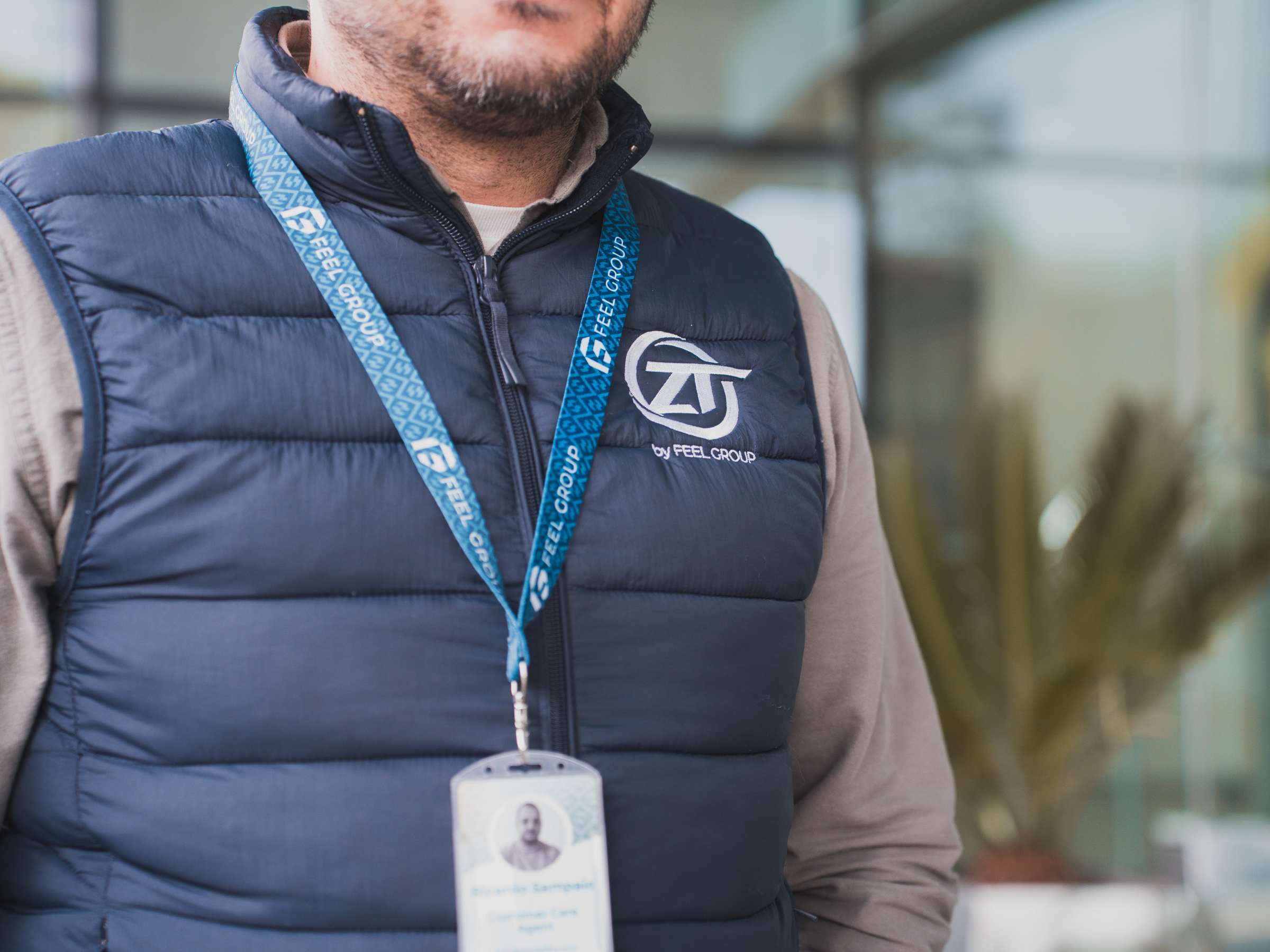 Man in blue vest with logo, wearing lanyard, outdoors.