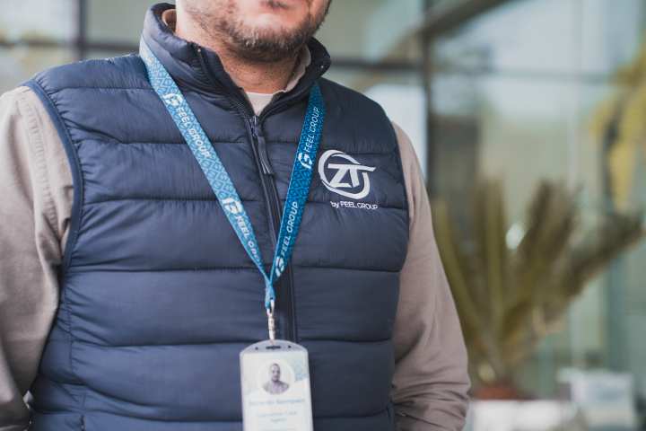 Man in blue vest with logo, wearing lanyard, outdoors.