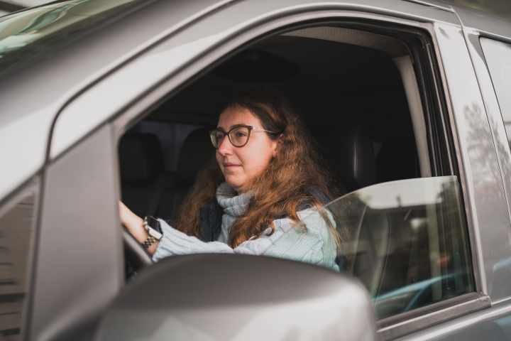 Person wearing glasses driving a car, looking forward through the open window.