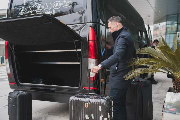 Man loading luggage into an open van trunk at a sidewalk.