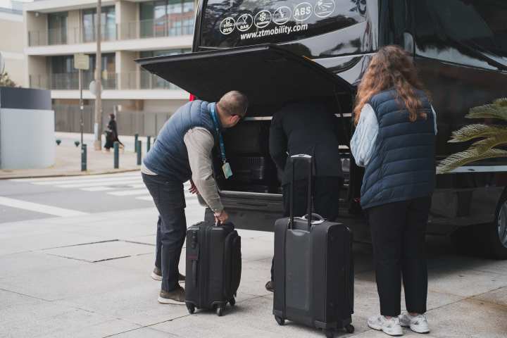 Three people loading luggage into a black van on a city street.