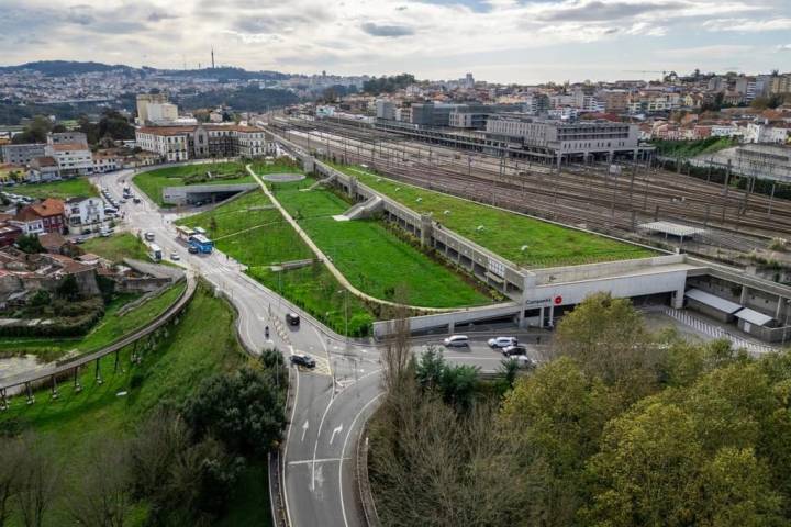 Aerial view of urban railway station with grass-covered roofs and surrounding roads.